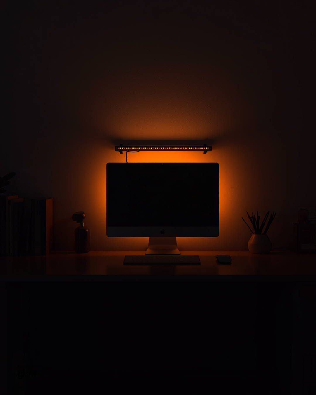 Dark home office with an amber USB LED light bar glowing above a monitor on a desk